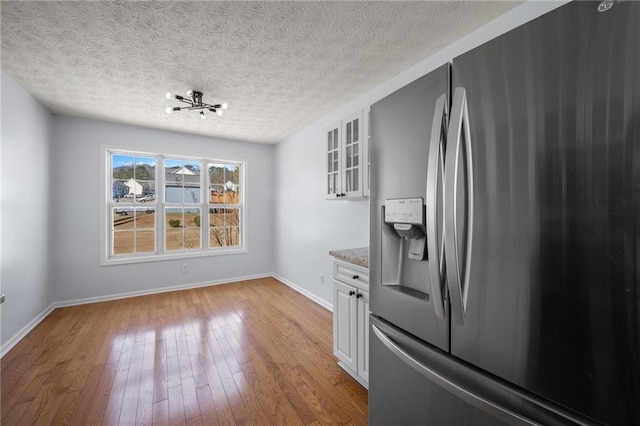 kitchen with glass insert cabinets, light wood-style floors, white cabinets, stainless steel fridge, and baseboards