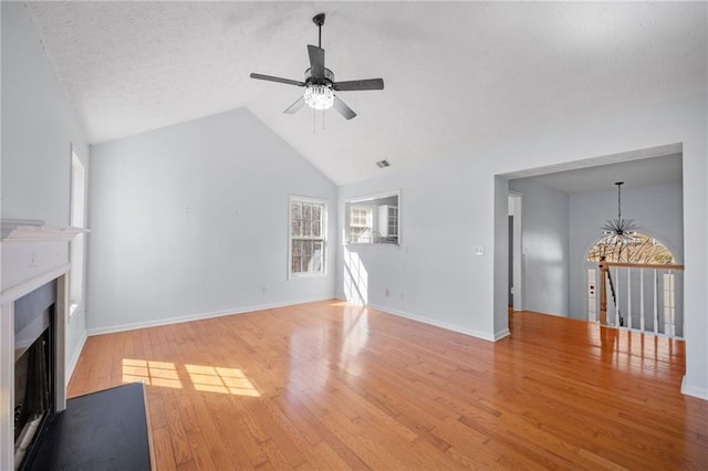 unfurnished living room featuring ceiling fan with notable chandelier, a fireplace, visible vents, vaulted ceiling, and light wood-type flooring