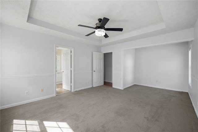 unfurnished bedroom featuring baseboards, a raised ceiling, a ceiling fan, connected bathroom, and carpet flooring