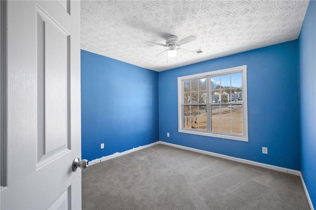 carpeted spare room with ceiling fan, visible vents, baseboards, and a textured ceiling