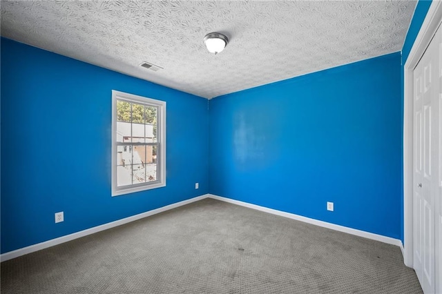 unfurnished room featuring a textured ceiling, carpet, visible vents, and baseboards