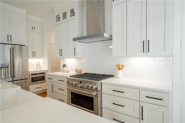 kitchen with white cabinets, wall chimney exhaust hood, decorative backsplash, and premium appliances