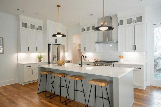 kitchen featuring high quality fridge, an island with sink, hanging light fixtures, and white cabinets