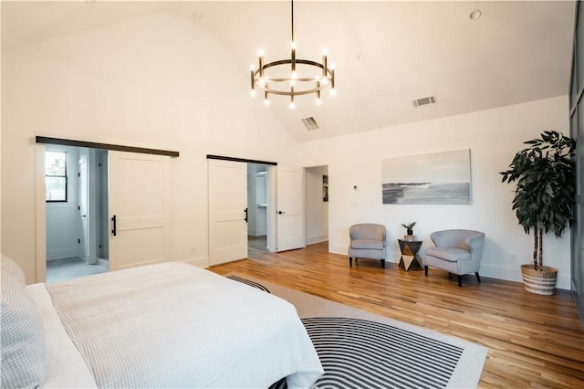 bedroom featuring an inviting chandelier, two closets, light hardwood / wood-style flooring, and high vaulted ceiling