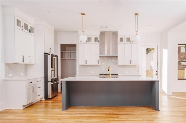 kitchen with high end fridge, white cabinetry, pendant lighting, light hardwood / wood-style floors, and wall chimney range hood