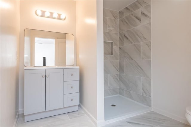 bathroom with a tile shower, vanity, baseboards, and toilet