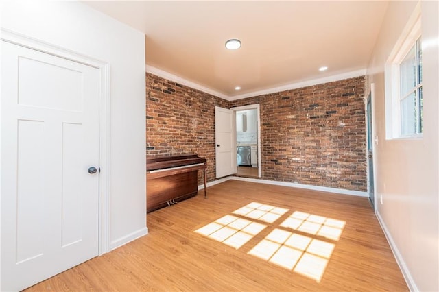 empty room with light wood-style floors, brick wall, baseboards, and ornamental molding
