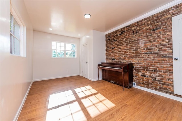 spare room with brick wall, recessed lighting, light wood-style floors, and baseboards