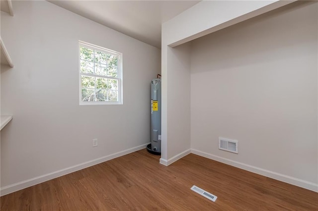 unfurnished room with water heater, visible vents, baseboards, and wood finished floors