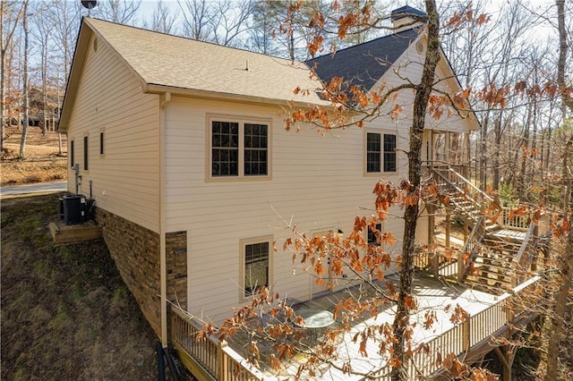 exterior space with a shingled roof, stone siding, a chimney, and stairs