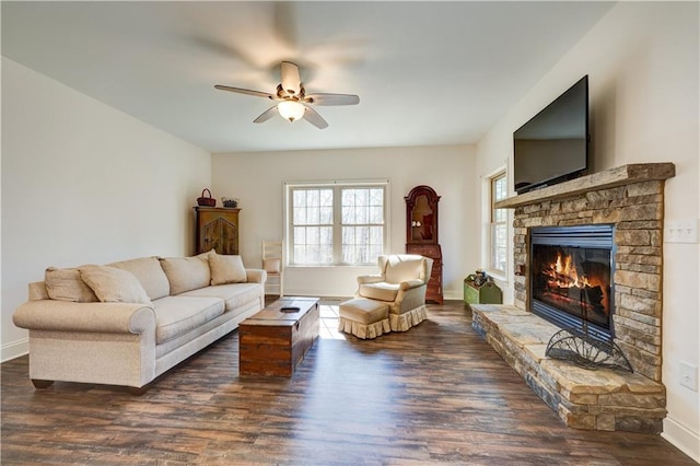 living room featuring a stone fireplace, wood finished floors, a ceiling fan, and baseboards