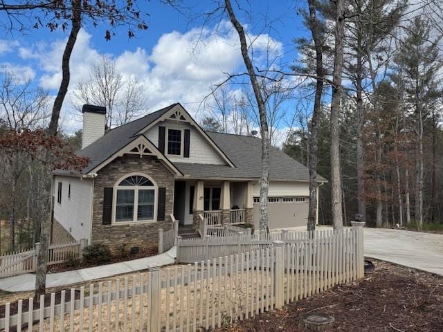 view of front facade with a garage, stone siding, a fenced front yard, and concrete driveway