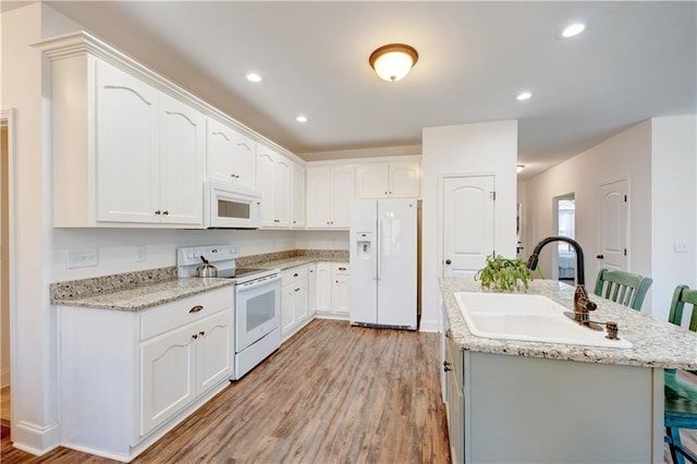 kitchen featuring white appliances, a kitchen island with sink, white cabinetry, and a sink