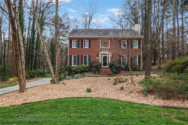 colonial house with brick siding, a chimney, and a front lawn