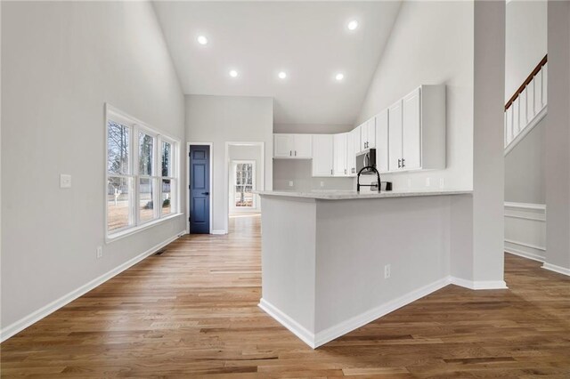 kitchen featuring high vaulted ceiling, sink, white cabinets, kitchen peninsula, and light wood-type flooring