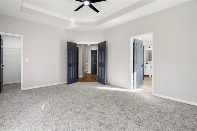 unfurnished bedroom featuring ceiling fan, a spacious closet, a raised ceiling, and ensuite bath