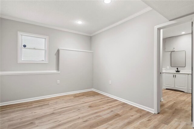 empty room featuring crown molding, sink, and light wood-type flooring