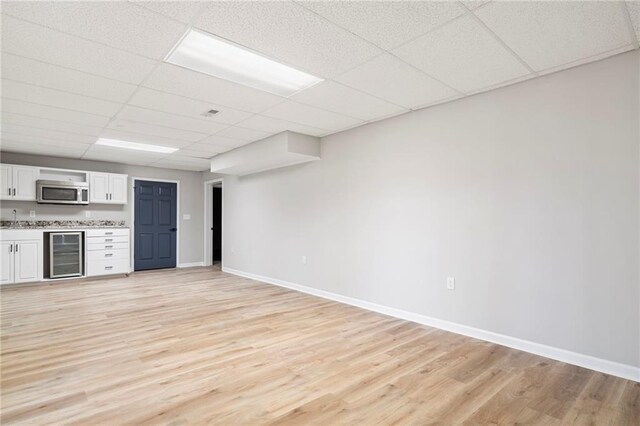 kitchen with white cabinets, a paneled ceiling, wine cooler, and light hardwood / wood-style floors