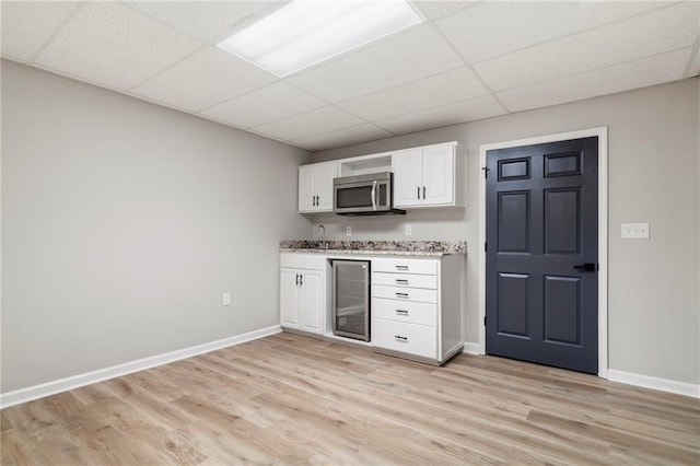 kitchen with sink, white cabinets, beverage cooler, light hardwood / wood-style floors, and a drop ceiling