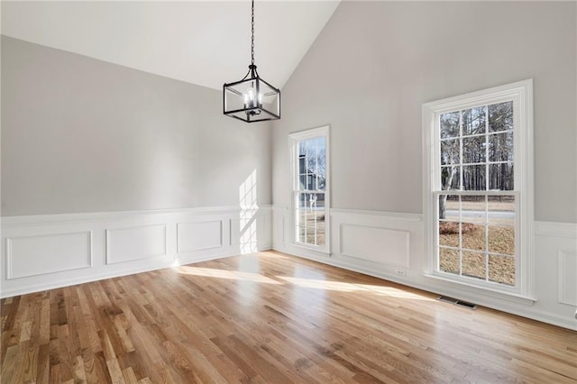 unfurnished dining area with lofted ceiling, an inviting chandelier, and light wood-type flooring