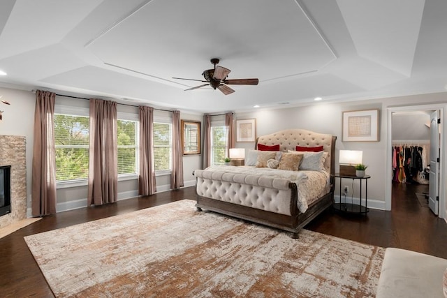 bedroom featuring a stone fireplace, ceiling fan, a raised ceiling, a closet, and a walk in closet