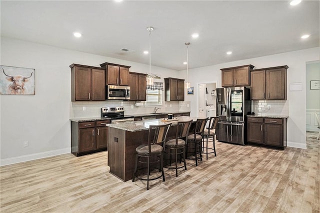kitchen with stainless steel appliances, light wood-style flooring, a kitchen bar, and dark brown cabinets