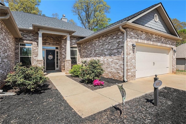 view of exterior entry with roof with shingles, brick siding, an attached garage, a chimney, and driveway