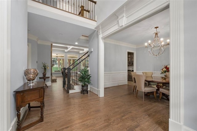 entrance foyer featuring stairs, wood finished floors, a chandelier, crown molding, and wainscoting