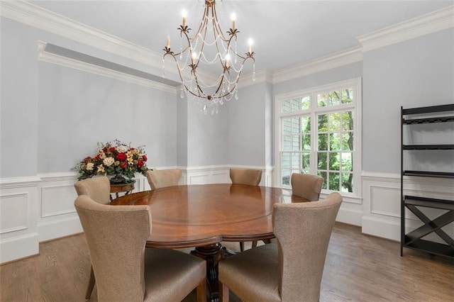 dining room with a chandelier, wood finished floors, ornamental molding, a decorative wall, and a wainscoted wall