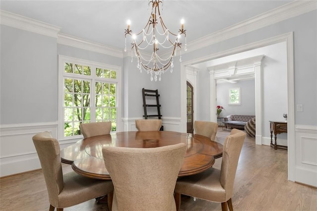 dining space with light wood finished floors, crown molding, a chandelier, and a wainscoted wall