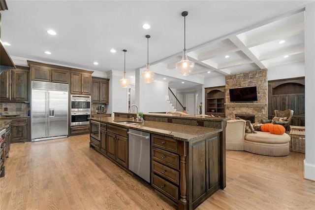 kitchen with appliances with stainless steel finishes, a sink, recessed lighting, light wood-type flooring, and a center island with sink