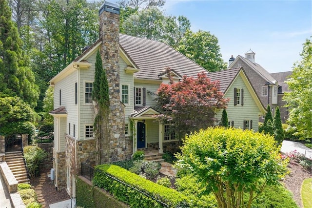 view of front facade featuring a chimney, stone siding, fence, and stairway