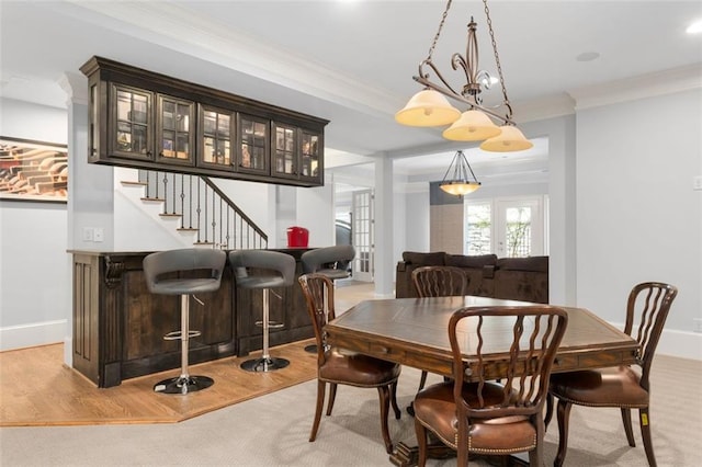 dining space featuring crown molding, a bar, wood finished floors, and baseboards
