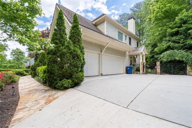 view of side of property featuring concrete driveway, a chimney, fence, and an attached garage