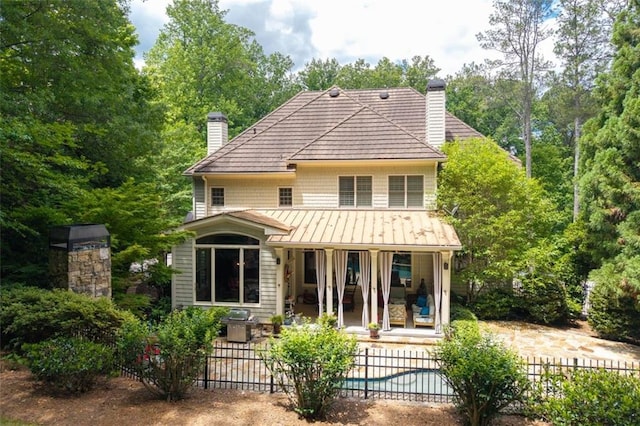 rear view of property with a chimney, fence, a patio, and a standing seam roof