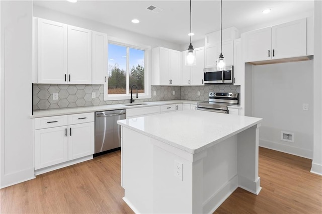 kitchen with sink, plenty of natural light, appliances with stainless steel finishes, pendant lighting, and white cabinets