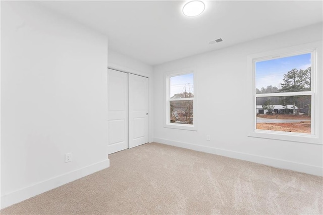 unfurnished bedroom featuring multiple windows, light colored carpet, and a closet