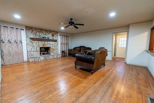 living room with hardwood / wood-style flooring, ornamental molding, a stone fireplace, and ceiling fan