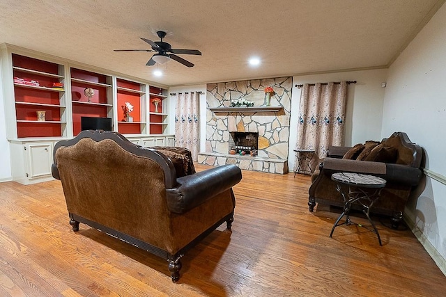 living room with light hardwood / wood-style flooring, ceiling fan, a fireplace, and a textured ceiling