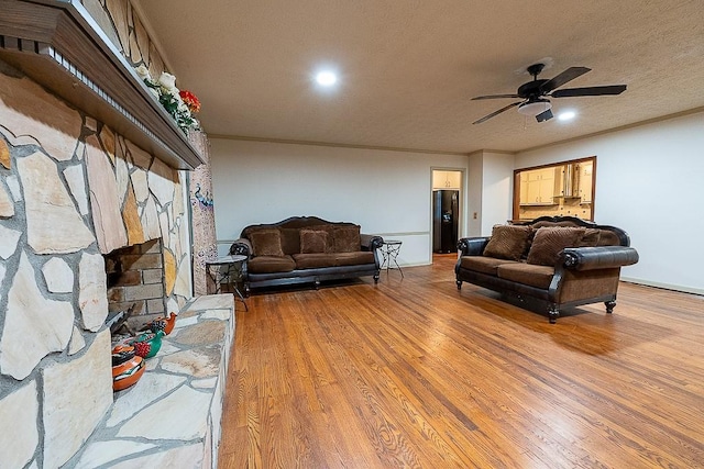 living room with crown molding, a stone fireplace, wood-type flooring, and a textured ceiling