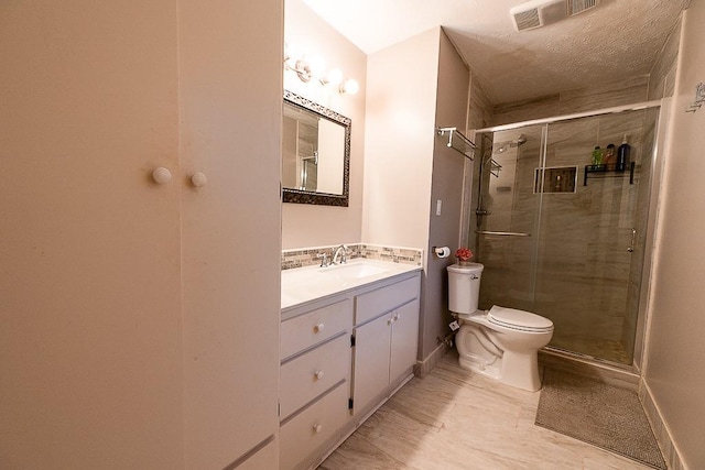 bathroom with vanity, a textured ceiling, a shower with shower door, and toilet