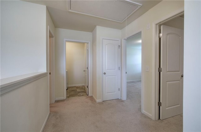 hallway with light colored carpet, attic access, and baseboards