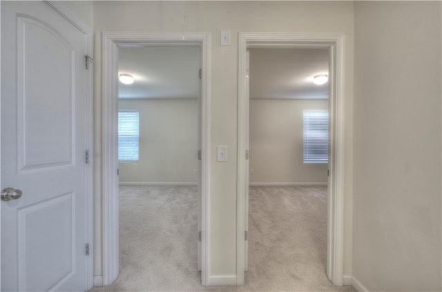 hallway with baseboards and light carpet
