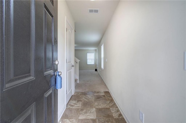 hallway featuring visible vents, baseboards, and stone finish floor