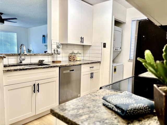 kitchen featuring white cabinetry, stainless steel dishwasher, stacked washer / drying machine, and sink