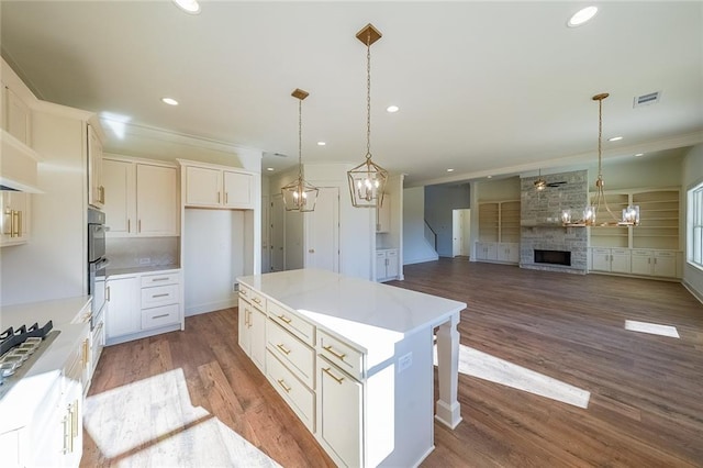 kitchen with white cabinets, a center island, decorative light fixtures, a fireplace, and ceiling fan