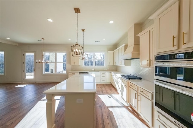 kitchen featuring pendant lighting, appliances with stainless steel finishes, custom exhaust hood, a kitchen island, and backsplash