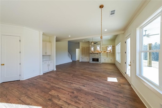 unfurnished living room featuring dark hardwood / wood-style flooring, a stone fireplace, ornamental molding, and a notable chandelier