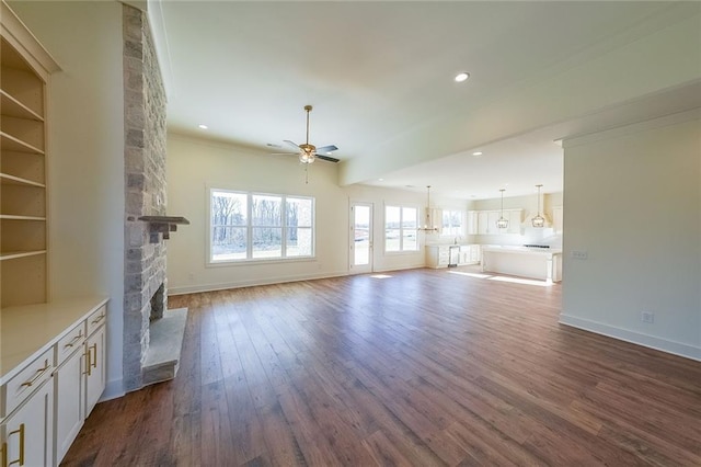 unfurnished living room featuring ceiling fan, dark wood-type flooring, crown molding, and a fireplace