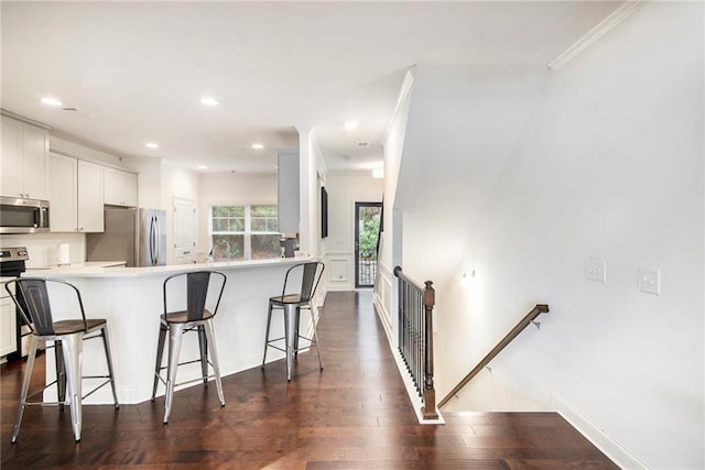 kitchen with a breakfast bar area, white cabinetry, stainless steel appliances, dark hardwood / wood-style flooring, and kitchen peninsula